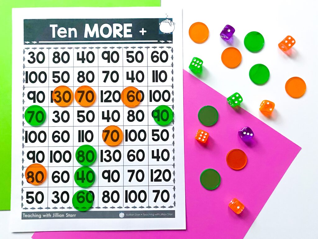 A math Halloween center where students roll dice and then add ten more to the sum. The game board, counters and dice are visible for this Halloween center.