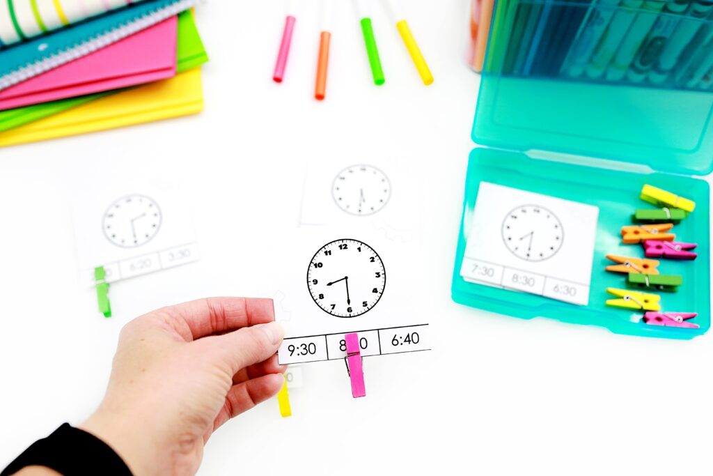 clip cards to review telling time to the half hour. Each card shows a clock face with a time to the half hour, and three possible digital clock options below. Students clip the card on the digital clock they think is a match.